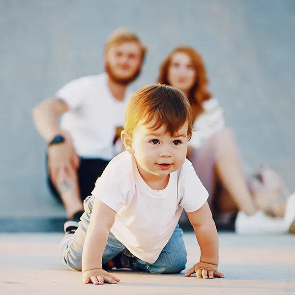Toddler crawling toward the camera with his parents sitting behind him