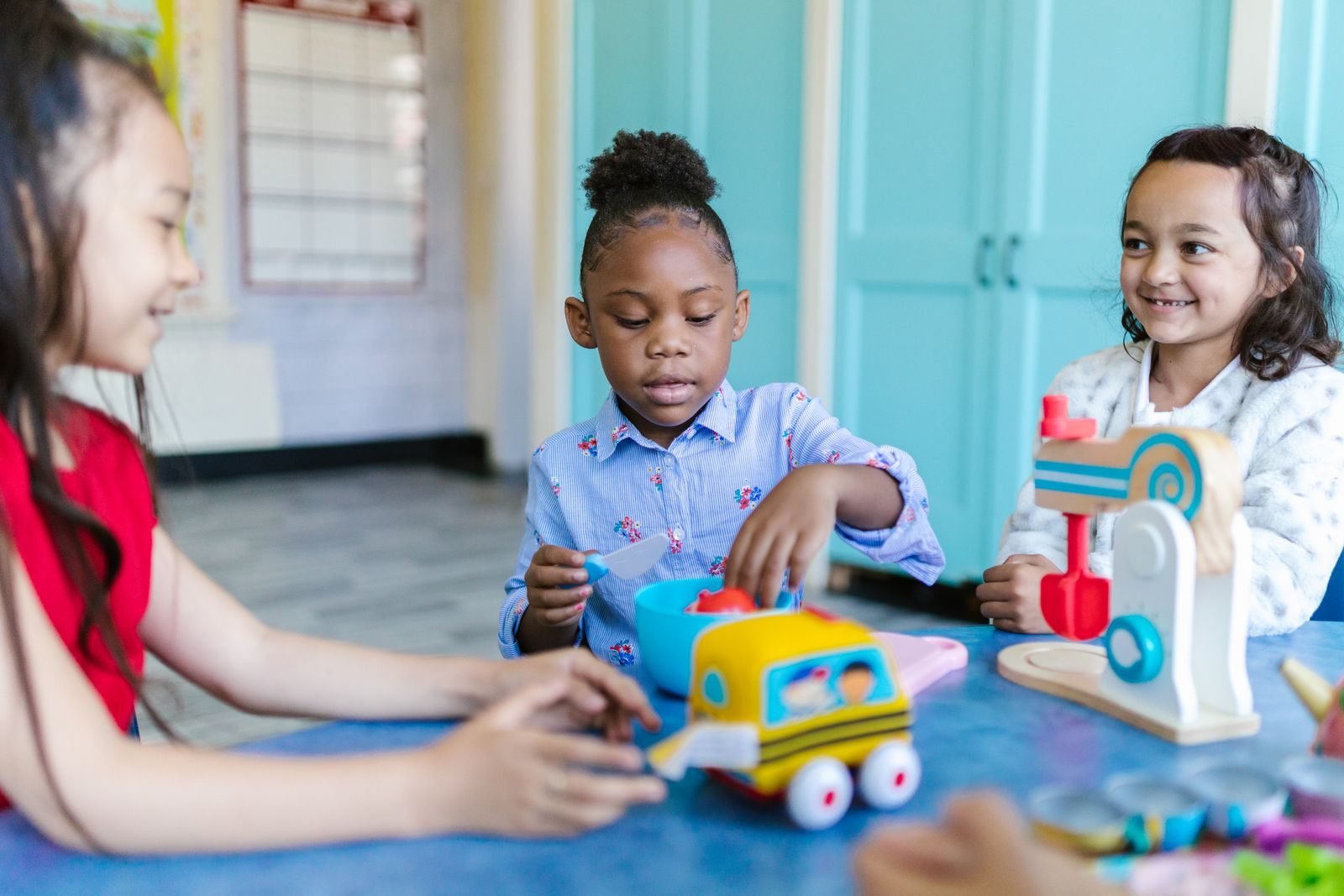 Three young girls playing together with toy cars and blocks at a classroom table