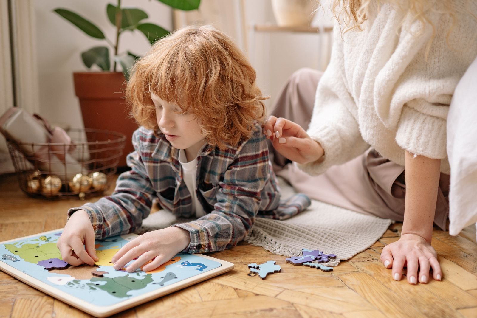 Young boy putting together a floor puzzle while his mother kneels beside him
