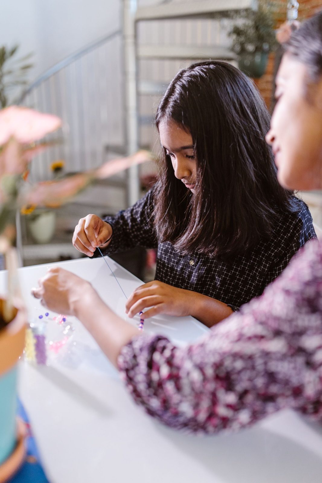 Girl threading beads onto a bracelet at a table with her mother